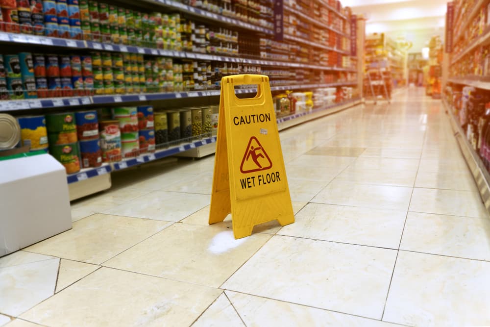 A cautionary yellow sign stands amidst the blur of supermarket shelves, warning of a wet floor.