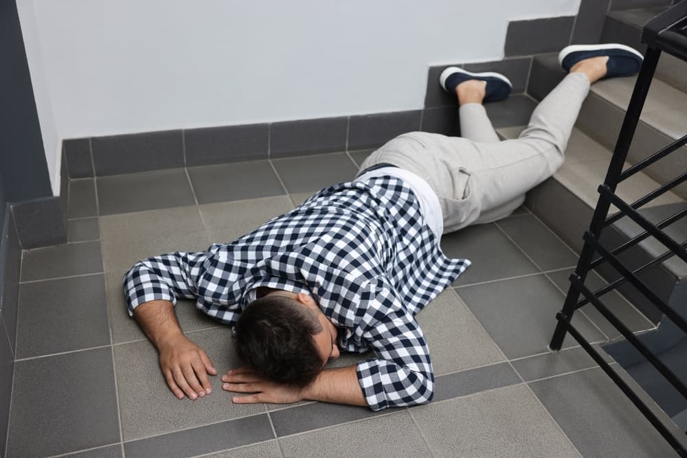 An unconscious individual is sprawled on the floor indoors after a fall down the stairs.