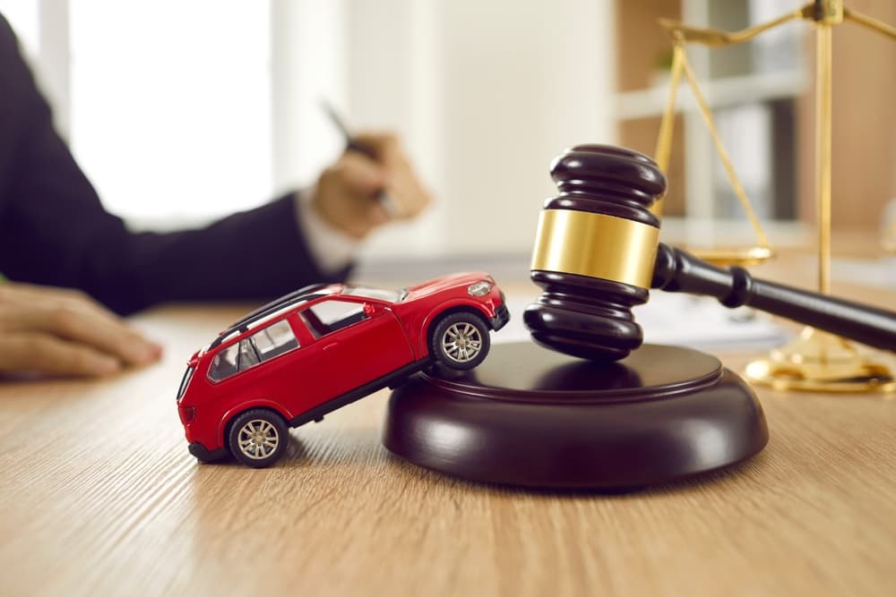 A small toy car on a gavel with scales of justice in background.